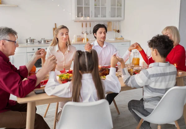 Big extended family holding hands at table, praying before Thanksgiving or Christmas dinner at home — Stock Photo, Image