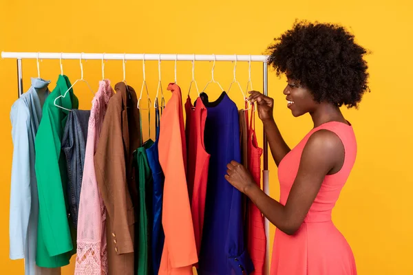 Africano Feminino em pé perto do vestuário cremalheira escolher roupa no estúdio — Fotografia de Stock