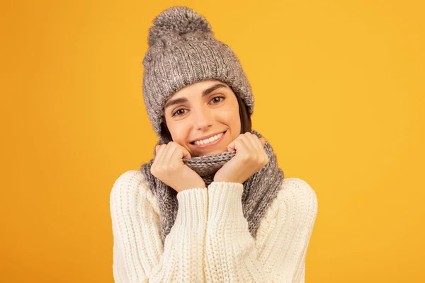 Feliz joven dama en gris conjunto de invierno, tocando bufanda, sonriendo y posando a la cámara sobre fondo de estudio amarillo —  Fotos de Stock