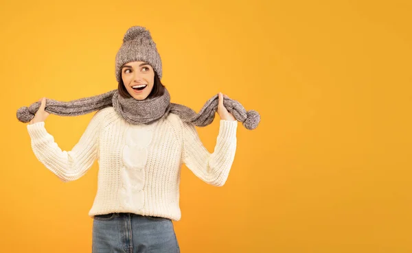 Cool oferta de invierno, promo. Emocionada dama en cálido traje de invierno, sonriendo y mirando el espacio libre sobre fondo amarillo —  Fotos de Stock