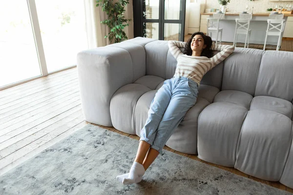 Avkopplande helgmorgon hemma. Glad ung kvinna vilar på bekväm soffa med slutna ögon, inomhus — Stockfoto