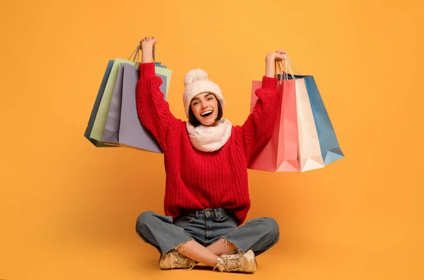 Sezónní prodej. Šťastná žena drží nákupní tašky, sedí na žlutém pozadí a usmívá se do kamery — Stock fotografie