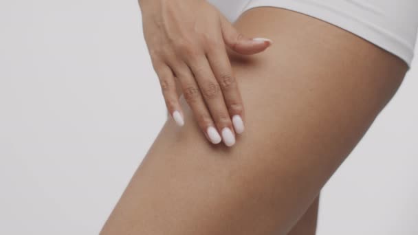 Антицелюлітний догляд за тілом. Африканська американка намазує вершки на стегнах, дбаючи про стан шкіри. — стокове відео