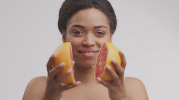 Mujer afroamericana joven dividiendo toronja en mitades y sonriendo a la cámara, fondo blanco del estudio, cámara lenta — Vídeo de stock