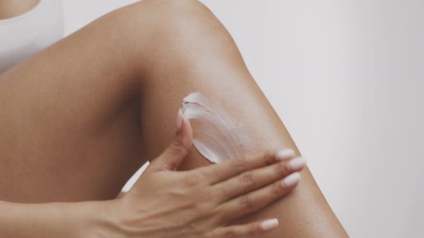 Mimos corporales después de depilación. Primer plano de mujer afroamericana irreconocible aplicando crema nutritiva en las piernas — Vídeo de stock