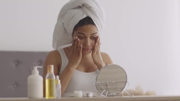 Una rutina de belleza matutina. Joven mujer afroamericana haciendo levantamiento de la piel masaje facial, mirando el espejo en el dormitorio — Vídeos de Stock