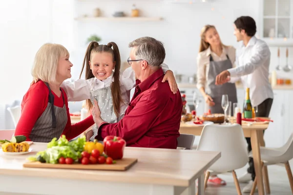 Amare i nonni abbracciando la loro nipote carina mentre cucinano la cena festiva a casa — Foto Stock