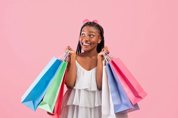 Feliz joven negra con bolsas de compras comprando regalos a la venta sobre fondo de estudio rosa. Descuento estacional —  Fotos de Stock