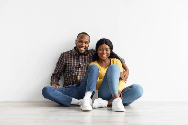 Retrato de casal afro-americano alegre sentado no chão perto da parede branca — Fotografia de Stock