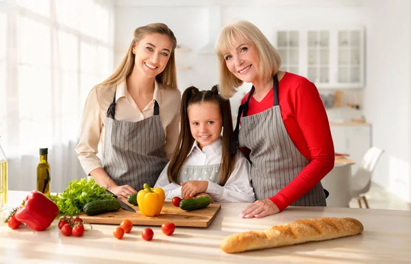 Çok nesilli aile portresi, sevimli bir kız, annesi ve büyükannesi mutfakta poz veriyor, kameraya gülümsüyor. — Stok fotoğraf