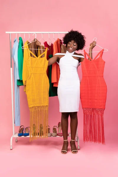 Africano Senhora Fazendo Compras Segurando Dois Vestidos, Fundo Rosa, Vertical — Fotografia de Stock
