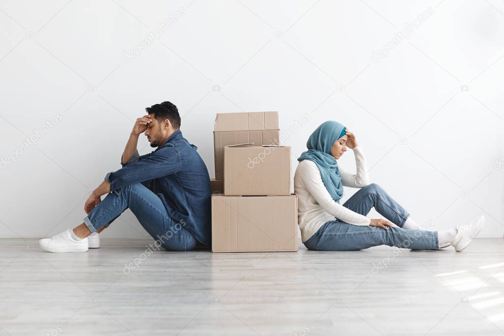 Upset middle-eastern family sitting separated by paper boxes on floor