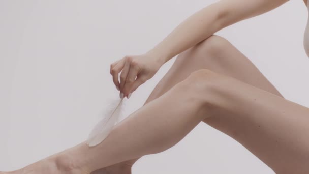 现代脱毛。一个无法辨认的高加索女人用羽毛爱抚着她完美腿的光滑皮肤 — 图库视频影像