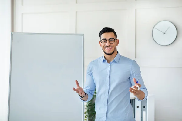 Fröhliche junge arabische männliche Lehrer geben Online-Privatunterricht von zu Hause aus, stehen in der Nähe leere Tafel mit Attrappe — Stockfoto