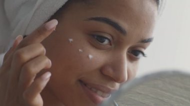 Günlük güzellik hizmetleri prosedürleri. Genç Afrikalı Amerikalı kadın göz altı bölgesine besleyici krem sürüyor.