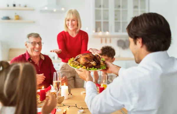 Joven sirviendo pavo de fiesta tradicional para una gran familia extendida, celebrando Acción de Gracias o Navidad en casa — Foto de Stock