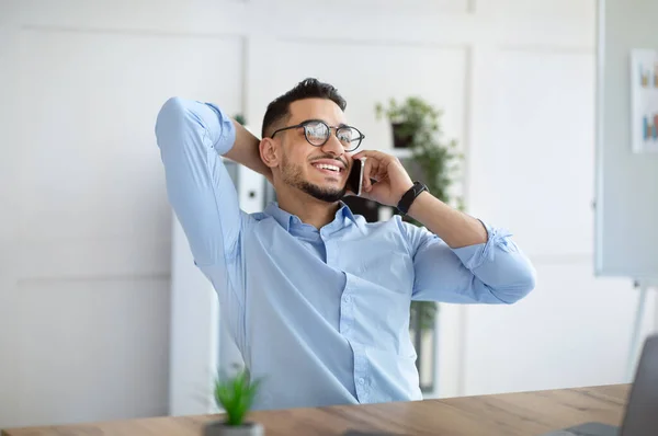 Atractivo joven árabe en ropa formal hablando en el teléfono inteligente en el lugar de trabajo. Concepto de comunicación empresarial —  Fotos de Stock