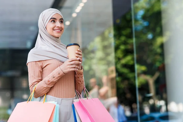 Sonriendo atractiva joven árabe hembra en hijab con un montón de bolsas con compras y taza de café — Foto de Stock