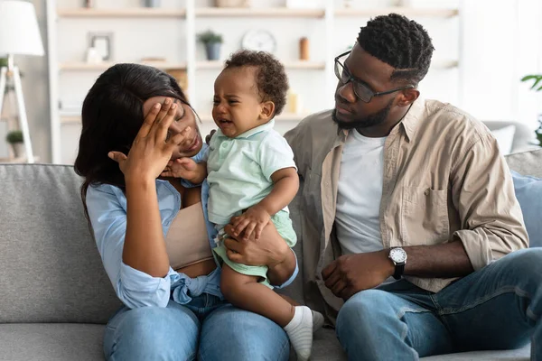 Tired African American parents sitting with crying kid on sofa — Stock Photo, Image