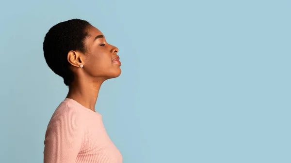 Profil einer jungen Afroamerikanerin, die mit geschlossenen Augen vor blauem Hintergrund steht — Stockfoto