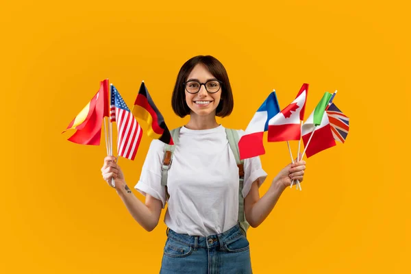 Happy lady showing bunch of diverse flags cheerfully smiling at camera over yellow studio background — Stock Photo, Image