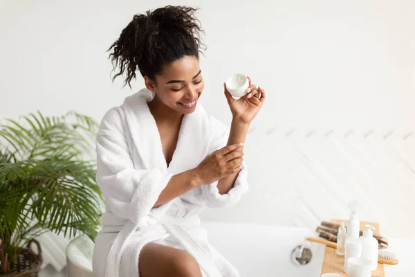 Femme noire appliquant la crème sur les bras et les coudes dans la salle de bain — Photo