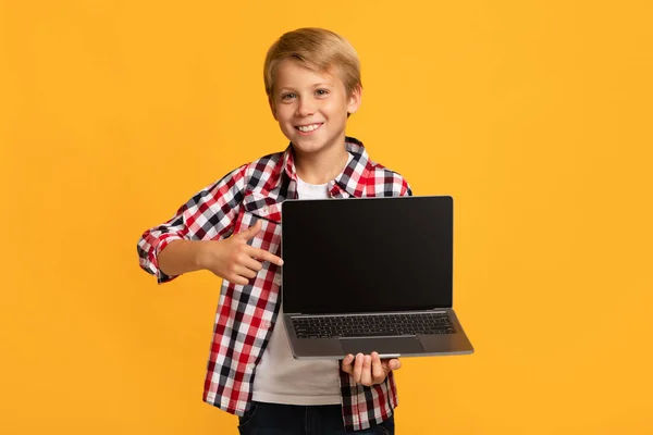 Szczęśliwy nastolatek blondynka chłopiec uczeń pokazać palec na laptop z pusty ekran — Zdjęcie stockowe
