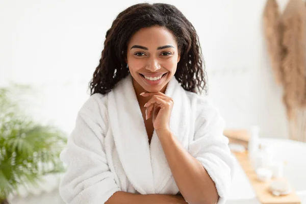 Zwarte dame poseren dragen witte badjas aanraken kin in de badkamer — Stockfoto