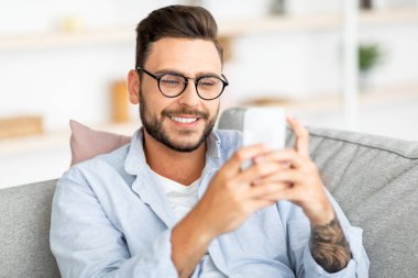 Ev içi rahatlık. Mutlu adam akıllı telefon kullanıyor ve oturma odasındaki koltukta dinleniyor.