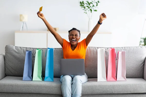 オンラインショッピング。興奮して叫んで手を上げて手を持ち上げインターネットで購入するクレジットカードやラップトップを持つアフロ女性 — ストック写真