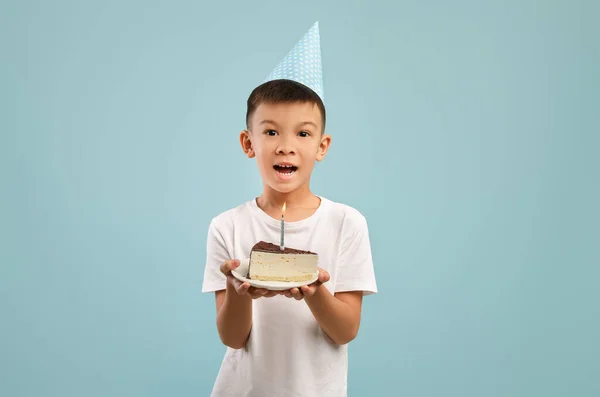 Menino asiático pequeno feliz no chapéu do partido que prende o bolo de aniversário com vela — Fotografia de Stock