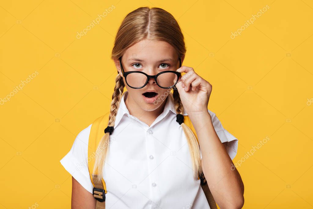 Surprised cute teenager caucasian blonde girl with pigtails and backpack, opens mouth takes off glasses