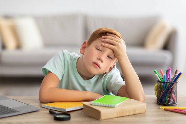 Evde dizüstü bilgisayarın önünde ödev yapmaktan sıkılan çocuk.