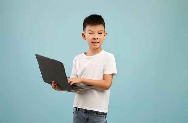 Концепция онлайн образования. Маленький азиатский мальчик с ноутбуком позирует над синим фоном — стоковое фото