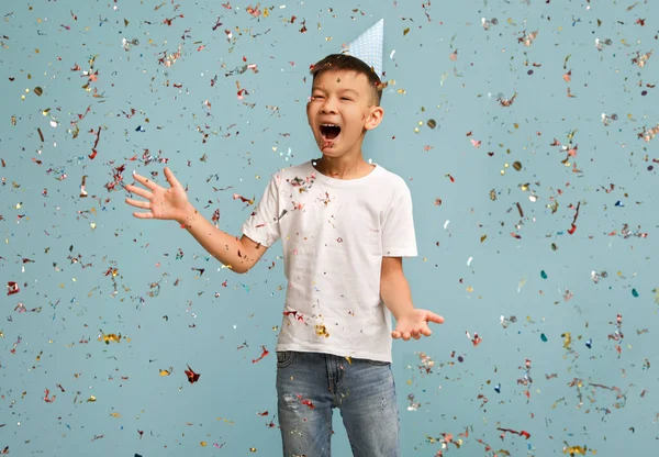 Doğum günü partisi. Doğum günü şapkası takan Mutlu Asyalı Çocuk Düşen Konfeti Altında Duruyor — Stok fotoğraf