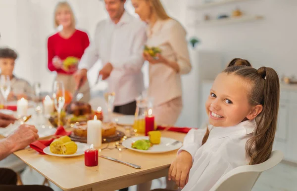 Adorable chica feliz sentada en la mesa festiva, celebrando las fiestas tradicionales con su gran familia en casa, espacio para copiar — Foto de Stock