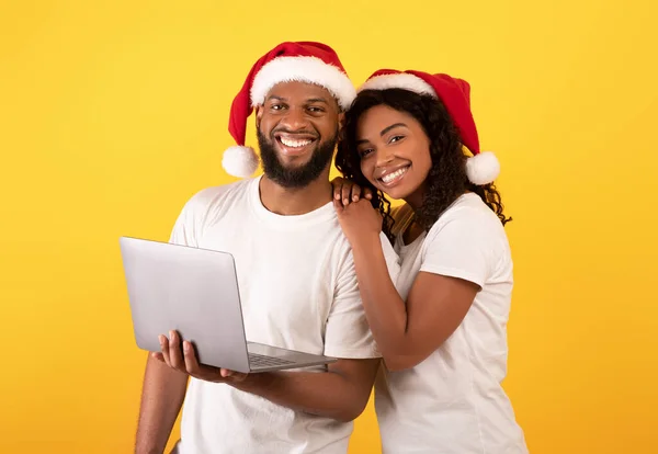 Online αγορές διακοπών. Χαρούμενη νεαρή αφροαμερικάνικη οικογένεια ποζάρει με laptop και χαμογελά στην κάμερα, κίτρινο φόντο — Φωτογραφία Αρχείου