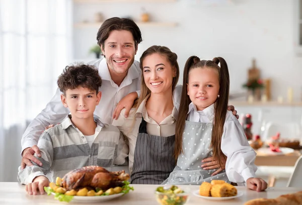 Padres jóvenes con hijo e hija sonriendo a la cámara, cocinando Acción de Gracias o cena de Navidad con pavo en la cocina — Foto de Stock