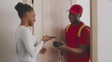 Neşeli Afrikalı Amerikalı kadın yemek siparişini cep telefonsuz ödeme uygulaması ve çanta ile ödüyor.