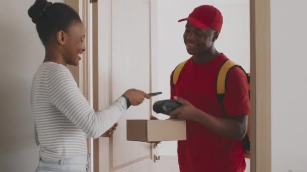 Νεαρή Αφροαμερικανή γυναίκα πληρώνει για την παραγγελία με smartphone και να πάρει το πακέτο κουτί από τον ταχυδρομικό υπάλληλο — Αρχείο Βίντεο