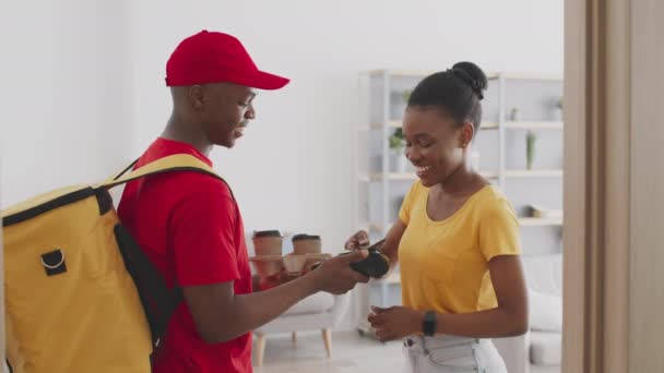 Muda african american ceria wanita membayar untuk kurir dengan smartphone dan mendapatkan pesanan kopi pada akhir pekan pagi — Stok Video