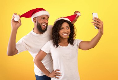 Xmas ve yeni yıl birlikte. Neşeli Afrikalı Amerikalı eşler Noel Baba şapkalarıyla eğleniyor ve selfie çekiyor.