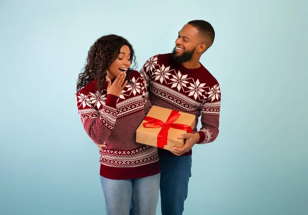 黒人男性を愛するクリスマスの贈り物に驚きの妻を祝います一緒にクリスマス,青の背景の上に立って — ストック写真