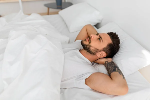 Gedachten in het hoofd laten niet in slaap vallen. Millennial man liggend in bed en kijkend naar het plafond, denken aan iets — Stockfoto