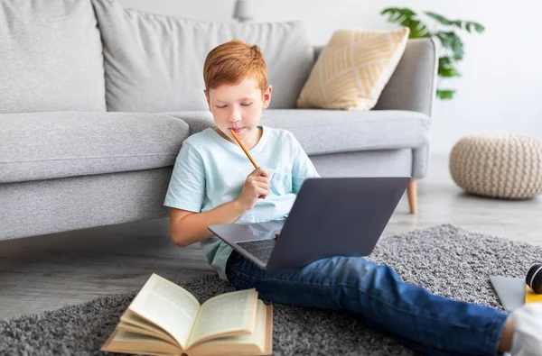 Счастливый студент рыжий мальчик с ноутбуком делает домашнее задание дома — стоковое фото