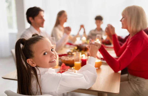 Niña feliz con la familia rezando antes del Día de Acción de Gracias festivo o la cena de Navidad, celebrando las vacaciones en casa — Foto de Stock