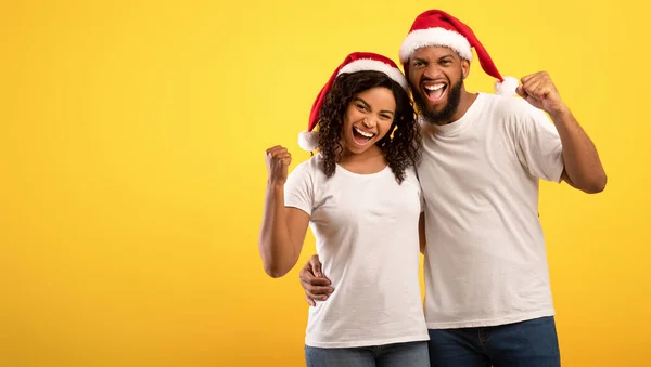 Överlycklig afrikansk amerikansk par i Santa hattar skakar nävar i spänning, poserar över gul bakgrund, fritt utrymme — Stockfoto