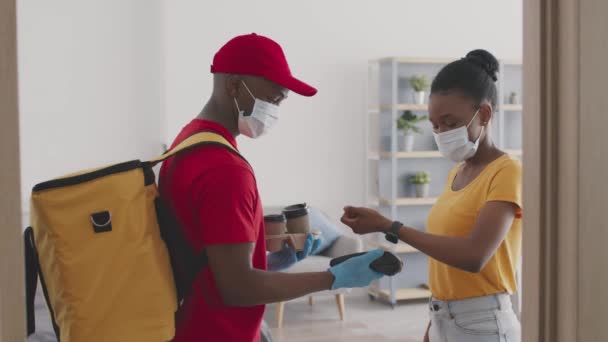 Africain américain livreur homme portant un masque de protection et des gants donnant du café à dame, femme noire en utilisant smartwatch — Video