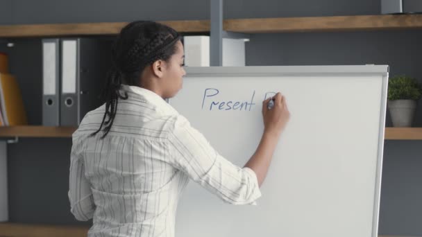 Clases de inglés. Vista posterior del profesor de lengua extranjera afroamericano profesional escribiendo tema en pizarra blanca — Vídeo de stock