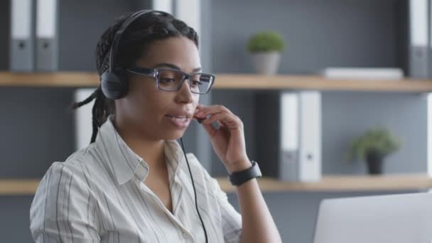 Junge selbstbewusste afrikanisch-amerikanische Callcenter-Betreiberin mit Headset im Gespräch mit Kunden per Videochat auf Laptop — Stockvideo